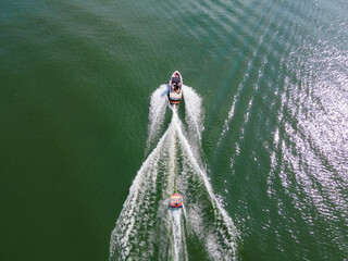 Wakeboard boat that is pulling a tube with people on it. Tubing on a wide open lake in summer time.