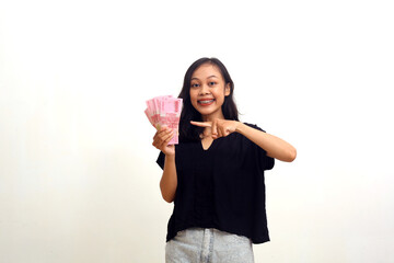 Happy asian young woman standing while holding and pointing indonesian money.