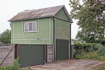Fototapeta na wymiar private green house with a window and a garage on the street with a gray concrete fence and metal gates