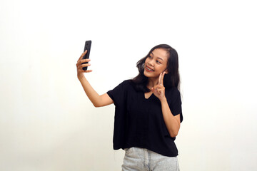Cheerful asian young woman doing self photograph with her cell phone. Isolated on white background