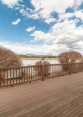 Vertical White puffy clouds Wooden deck with a view of dry shrubs and white fence against the and bright blue sky with clouds