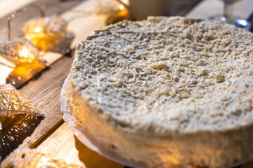 Cake with coconut chips on a wooden table against the background of a Christmas tree