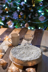 Cake with coconut chips on a wooden table against the background of a Christmas tree