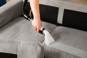 Man removing dirt from grey sofa with vacuum cleaner in room, closeup