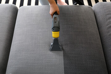 Woman removing dirt from sofa with vacuum cleaner at home, top view