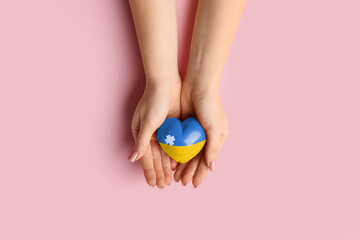 Fototapeta premium Female hands holding heart in colors of Ukrainian flag on pink background