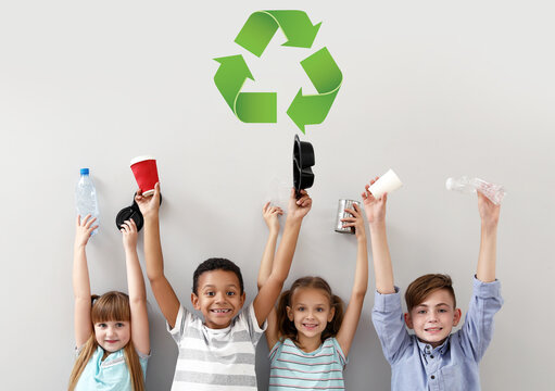 Little children with different trash and symbol of recycling on light background