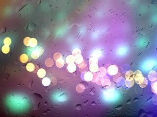 blurred pink blue yellow green light on rainy drops window glass 