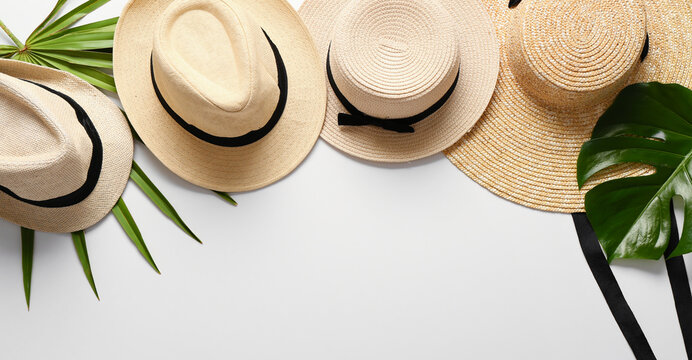 Summer straw hats with tropical leaves on light background with space for text