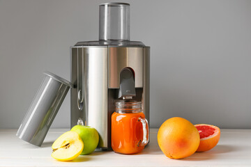 New modern juicer and mason jar of fresh juice with fruits on table
