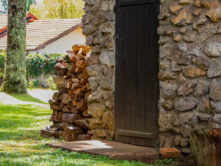 Traditional stone housing with wooden  door, and a pile of logs against a wall