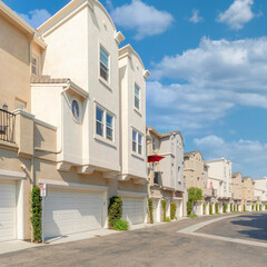 Square White puffy clouds Cream colored townhouses with attached garage asphalt driveway