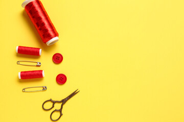 Thread spools, scissors, buttons and pins on yellow background