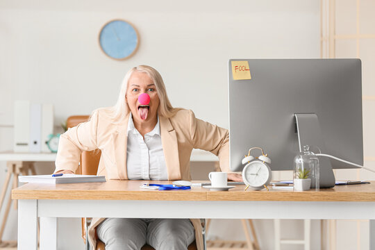 Funny mature woman with clown nose in office. April fools day celebration