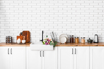 Sink with beautiful flowers and kitchen utensils on counters near white brick wall