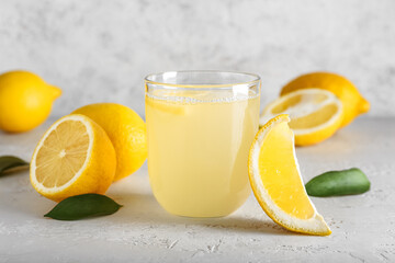 Ripe lemons and glass of fresh juice on light background
