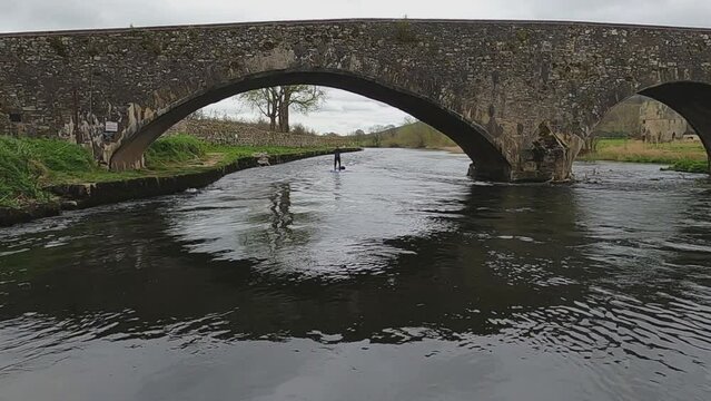 Paddleboarder paddles under old stone bridge near Tikincor Castle, IRE