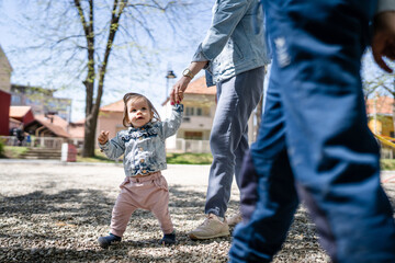 One baby small caucasian child little girl in park with her mother holding hand while assisting to walk in bright spring day real people childhood development learning and family concept copy space