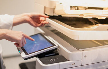 Female standing and hand pressing button on a copy machine in the office.