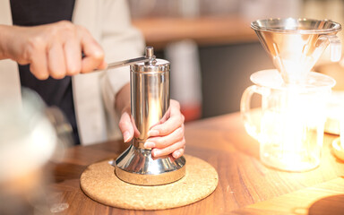 Female hand mash coffee bean in coffee grinder on wooden table.