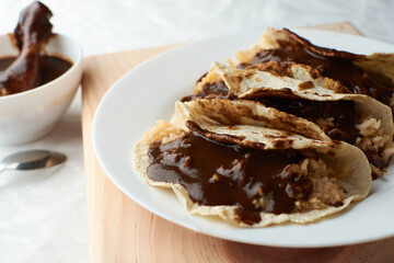 Tacos of mole with rice, placed on wood, in the background a piece of chicken