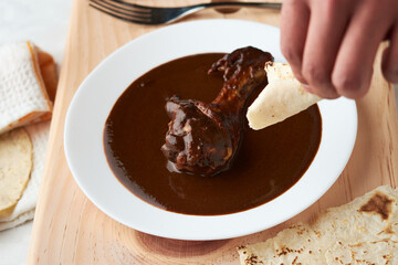 Chicken with mole, person taking a piece of tortilla, Mexican tradition, placed on wood
