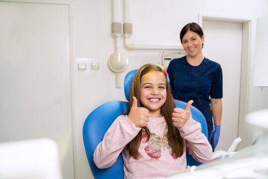 Little girl giving thumbs up and smiling while sitting in denist's chair 