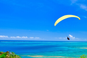 沖縄県知念岬のエメラルドグリーンの海を優雅に飛ぶパラグライダー