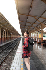 Obraz premium Portrait young Asian woman backpacker traveler walking alone at train station platform with backpack. Asian woman waiting train at train station for travel. Summer holiday traveling concept.