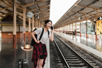 Beautiful young asian woman with a backpack uses the phone while standing near the railroad train on the platform. Cheap travel summer concept