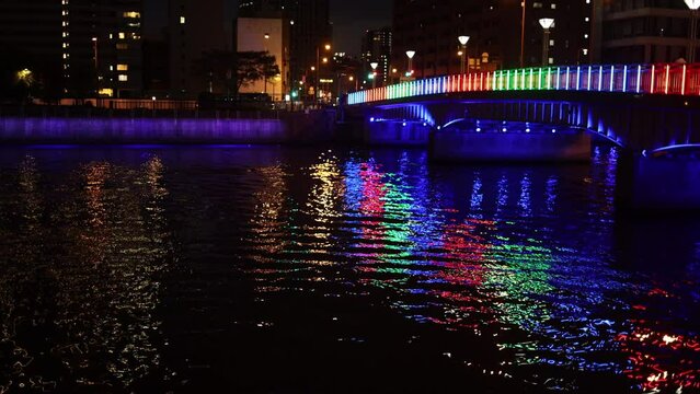 Colorful bridge reflects off ripples in river through city at night