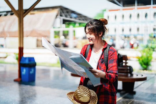 summer, relax, vacation, travel, portrait of a cute Asian girl looking at a map to plan a trip while waiting at the train station.