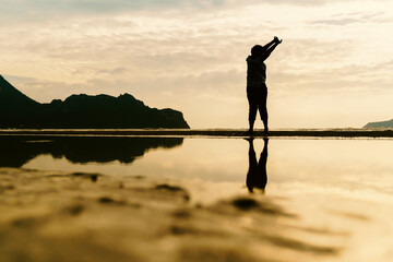 Asian Mature adult Woman doing stretching her hands in the air at sunrise or sunset beach silhouette