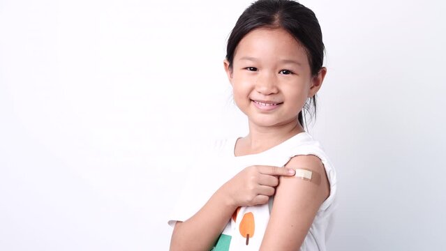 Vaccine concept. Happy Asian little child girl smiling, showing arm with plaster bandage after received, getting COVID-19 vaccine injection. Concept of inoculation, vaccinate, campaign, COVID19, Flu