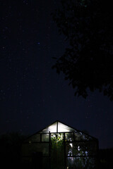Greenhouse with light under stary sky at night in village