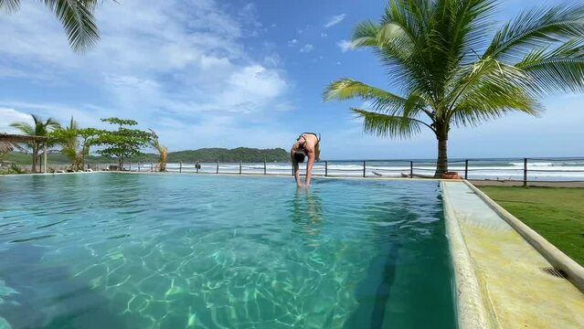SLOW MOTION: Young woman diving in infinity pool at tropical beach resort with oceanview. Female person enjoying summer days at exotic luxury resort in Panama. Refreshment on a hot summer day.