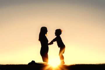 Fototapeta na wymiar Silhouette of Mother and Young Child Holding Hands at Sunset