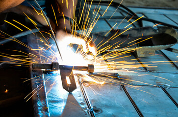 Welder is welding metal hook melting or fusing the two parts together by the heat. Weldment of a steel door. Long exposure of welding fires flares from the industrial welding factory