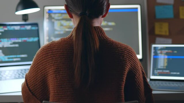 Young Asian woman, developer programmer, software engineer, IT support, wearing glasses working hard at night overtime on computer to check coding in bugging system. Back view
