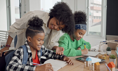 African American female teacher standing with pupils teaching writing lesson in modern classroom.