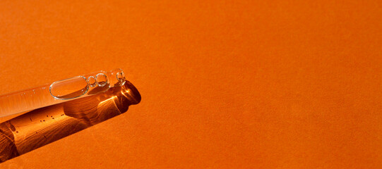 Pipette with serum or cosmetic liquid close-up on an orange background in soft focus. Beautiful...