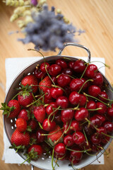 Large enameled colander with cherries and strawberries. The concept of summer and harvest. Top view.