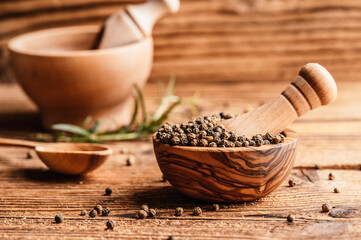 Black pepper in wood bowl on wooden table. Spices on desk. Organic spice dry peppercorn.