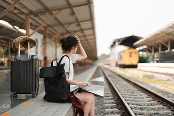 Young woman traveler with backpack looking to map while waiting for train, Asian backpacker on railway platform at train station. Holiday, journey, trip and summer summer travel concept