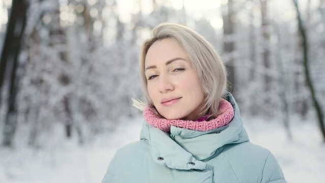 Portrait of a young woman in the winter forest. Pleasant blonde posing for the camera.