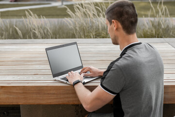 A young man or student or businessman is sitting at a table with a laptop with a black screen for text and typing on the keyboard.