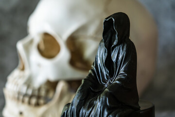 A statue of a grim reaper sitting and skull  background.