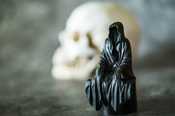 A statue of a grim reaper sitting and skull  background.