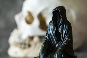 A statue of a grim reaper sitting and skull  background.