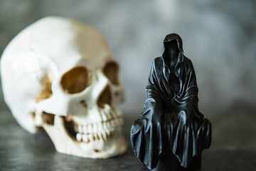A statue of a grim reaper sitting and skull  background.